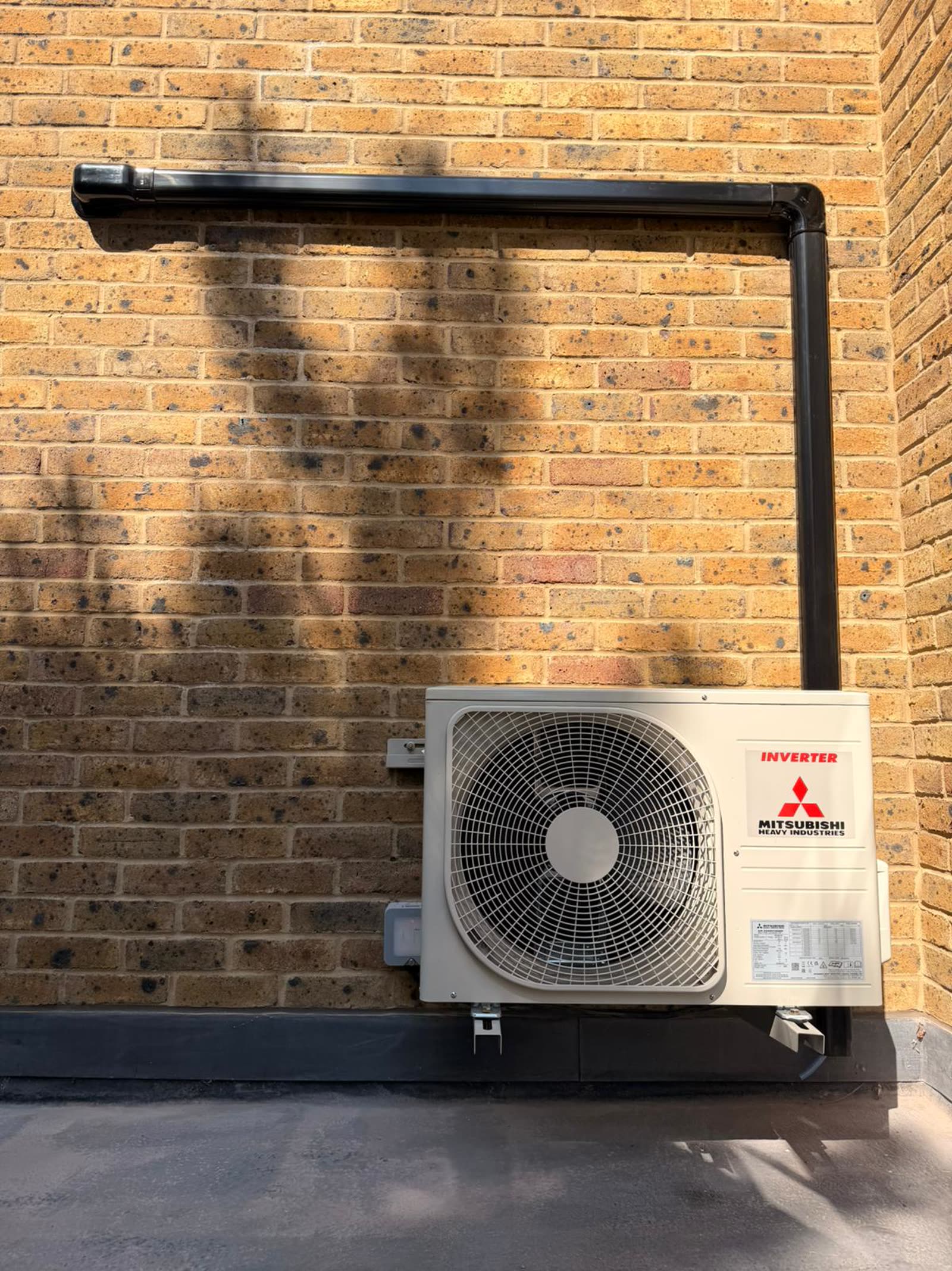 Mitsubishi Heavy Industries outdoor condenser on brackets with black trunking on a brick wall
