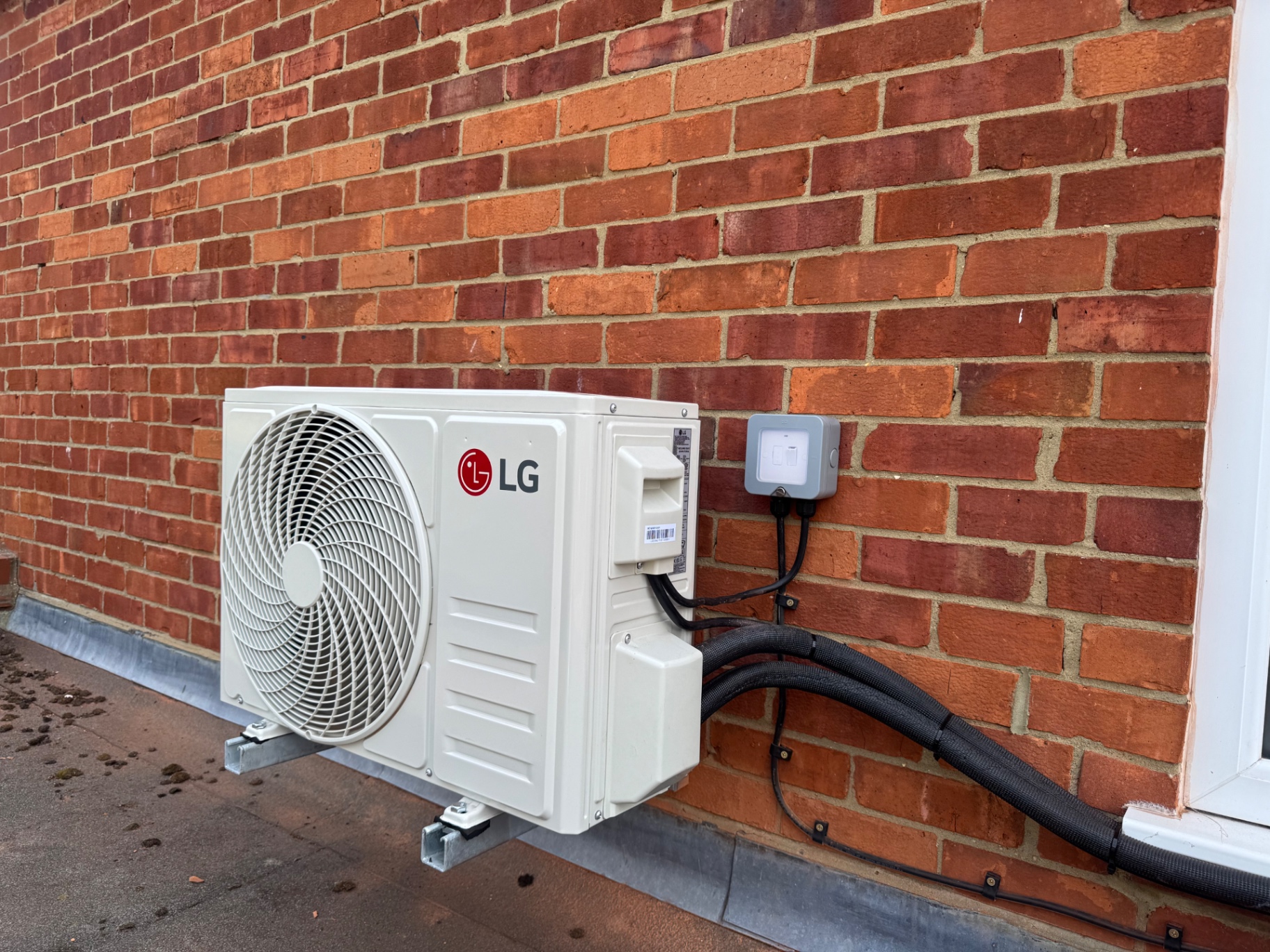 LG outdoor condenser unit wall-mounted on brackets against a brick wall with tidy trunking